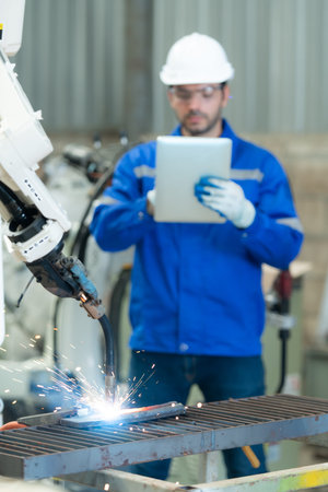 Young male engineers are manipulating a welding robot hand. By combining welding manipulation with a control panel for precise welding control. Rapid and very secureの写真素材