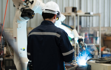 Young male engineers are manipulating a welding robot hand. By combining welding manipulation with a control panel for precise welding control. Rapid and very secureの写真素材