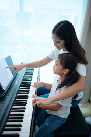 Family vacation, mother helping daughter practice in her piano lessons joyfully and happilyの写真素材