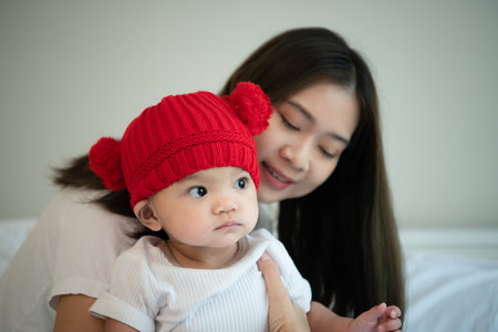 Mother and newborn baby wearing red hats In the white bedroom, warm sunlight in the evening of the day. Prepare to celebrate Christmasの写真素材