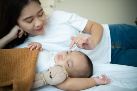 Young mother hugging her newborn child to lull the baby to sleep in the white bedroom, warm sunlight in the evening of the day.の写真素材