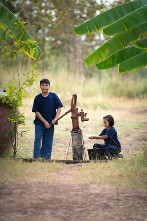 Childhood in rural Thailand. A small child assists his family by pumping natural water into a bucket to be used in everyday life