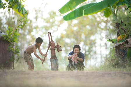 Childhood in rural Thailand. A small child assists his family by pumping natural water into a bucket to be used in everyday lifeの写真素材
