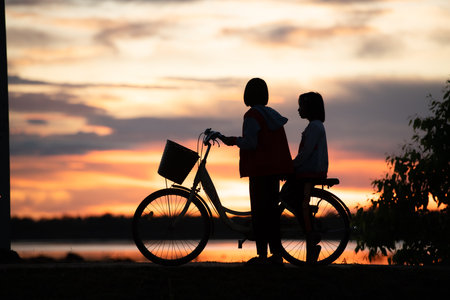Little girls riding bicycles in the early morning light of the day while the sun beams a stunning shade of orangeの写真素材