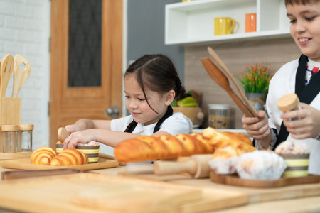 Portrait of a little girl and boy in the kitchen of a house having fun playing baking breadの写真素材
