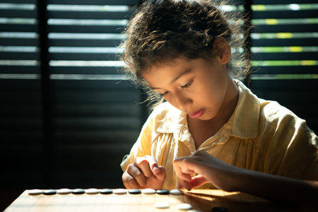 Portrait of a little girl in office room of house with a game of Go being learned to build...