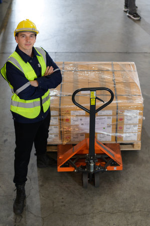 Worker in auto parts warehouse use a handcart to work to bring the box of auto parts into the storage shelf of the warehouse waiting for delivery to the car assembly lineの写真素材