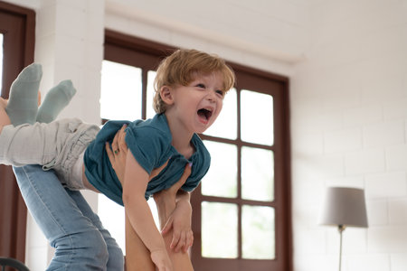 Little boy flying with mom using her legs to help him fly high off the floor of his bed in the bedroom.の写真素材