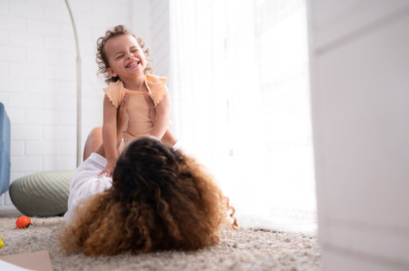 On a vacation morning, parents and children are having fun playing in the living room, with the father hoisting his daughter up behind her mother.の写真素材