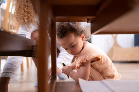 A little child's imagination is represented through colored pencil drawings, with the mother attentively supervising in the living room of the house.の写真素材