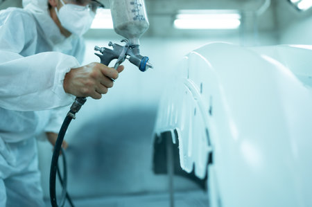 Auto mechanic in car spray room giving the spray nozzle injected into the car front bumper of the car with refinement in order to create beauty that blends with the original color of the carの写真素材