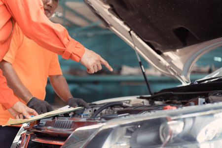 Both of auto mechanics are inspecting the engine of a customer's car being brought in for repair at a garage.の写真素材