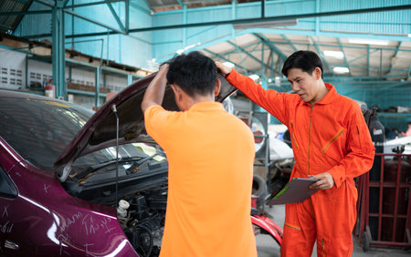 Both of auto mechanics are inspecting the engine of a customer's car being brought in for repair at a garage.の写真素材