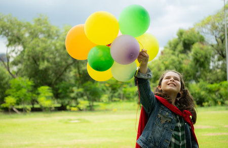 On a beautiful day in the park, a young girl enjoys her vacation. Playful with a red superhero costume and mask.の写真素材