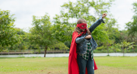 On a beautiful day in the park, a young girl enjoys her vacation. Playful with a red superhero costume and mask.の写真素材