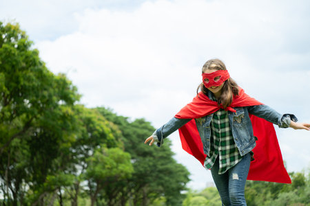 On a beautiful day in the park, a young girl enjoys her vacation. Playful with a red superhero costume and mask.の写真素材