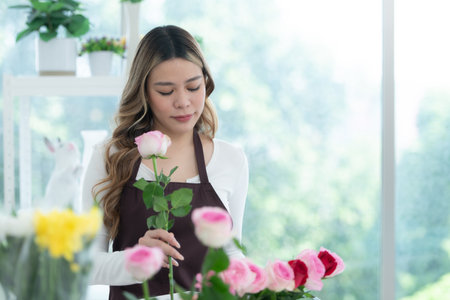 à¹Young woman florist smelling a red rose in the flower shopの写真素材