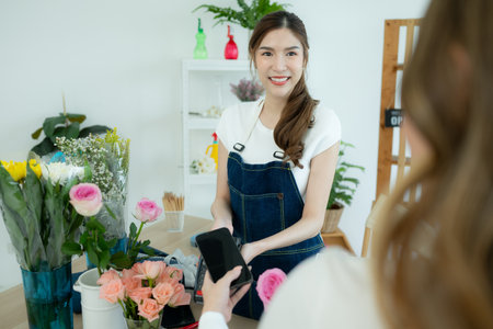 Cropped shot of female florist holding smartphone paying for flowers in flower shopの写真素材