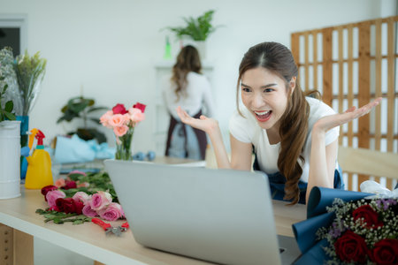 Young asian woman florist working with laptop in flower shop and glad that have orders immediately when the shop opens.の写真素材