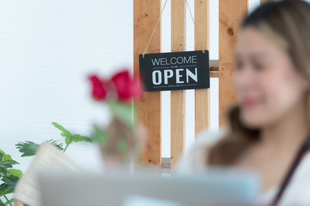 Woman using laptop with open sign in floral shop. Business concept.の写真素材