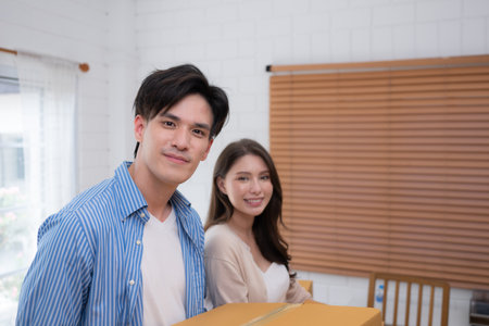 Young Asian couple carrying boxes in their new home. They are standing and smiling.の写真素材