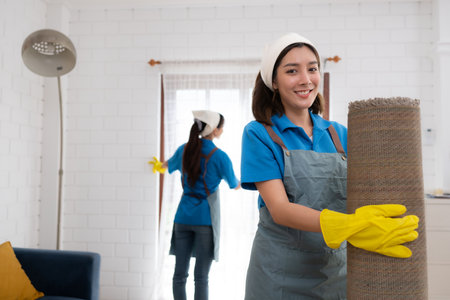 Young women cleaning maid in uniform and rubber gloves are cleaning the room, fold up carpetの写真素材