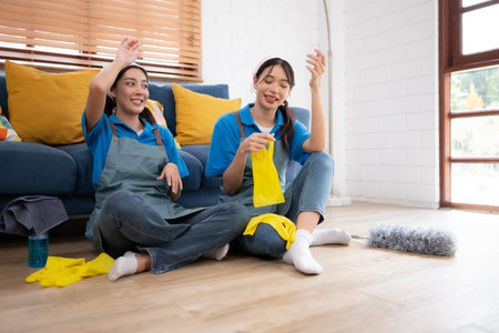Two young women in uniform cleaning the room while sitting on the floorの写真素材