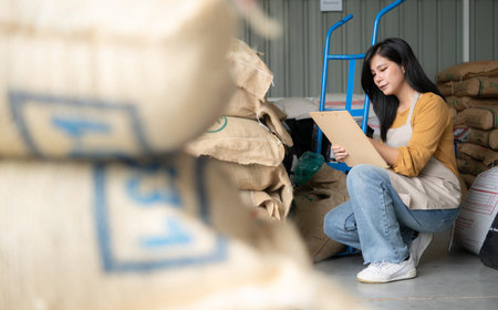 Young Asian woman sitting on the floor in coffee beans warehouse and checking documents