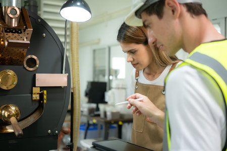 Portrait of young female warehouse worker talking with technician of coffee roaster machine  in...