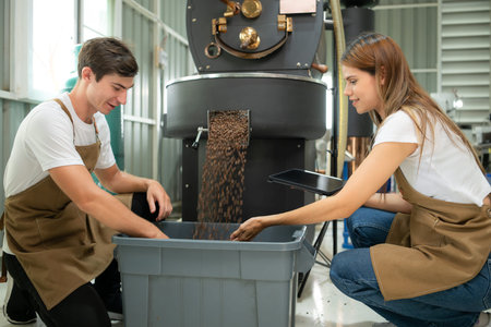 Young man and woman working in coffee beans roaster, They are checking of coffee beans roasted.