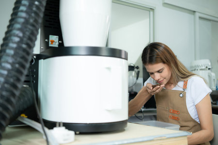 Young woman in apron using digital tablet for checking quality of of coffee beans with digital...