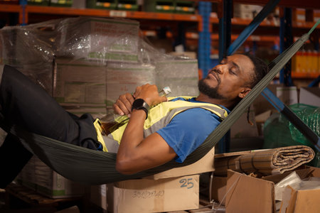 Portrait of young male worker relaxing in hammock with alcohol bottle in warehouse