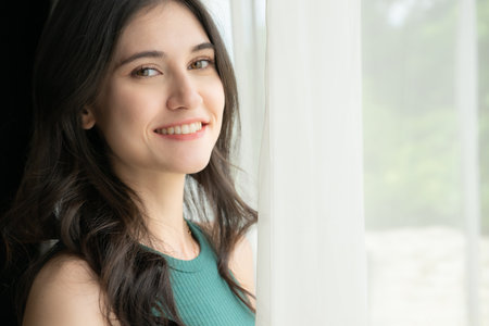 Portrait of a beautiful asian woman in green shirt standing near the windowの写真素材