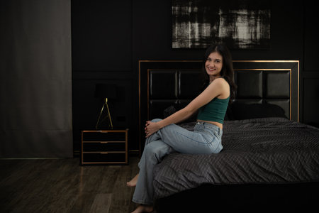 Young woman sitting on the bed in the room at night time.の写真素材