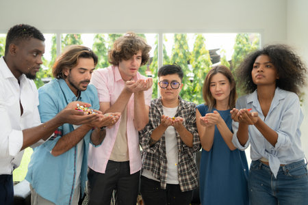 Group of multiethnic friends having fun at party playing fun blowing colorful paper