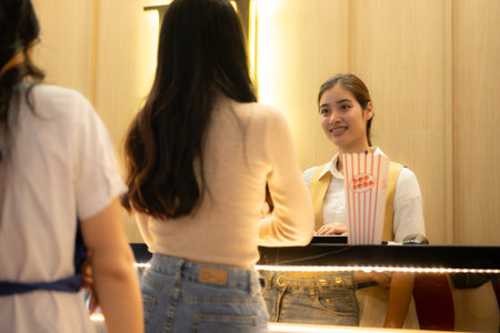 Young asian woman standing in line to buy movie tickets and in hand popcorn and drink, Smiling ticket salesman serving.の写真素材