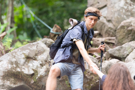 Young couple hiking in forest help each other in the climbing, Man and woman trekking in nature.