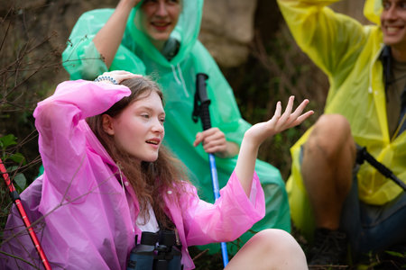 Group of friends in raincoat with backpacks hiking in the forest, Sit and shelter from the rainの写真素材