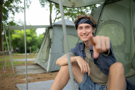 Young man sitting in front of tent at campsite in the countrysideの写真素材