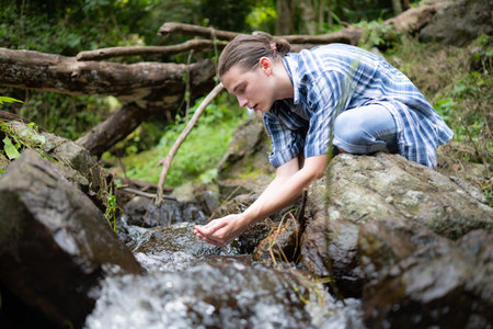 Hiker in the jungle playing with water in a stream in the forest.