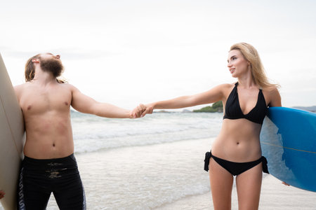 Couple of surfers holding hands and looking at each other on beachの写真素材