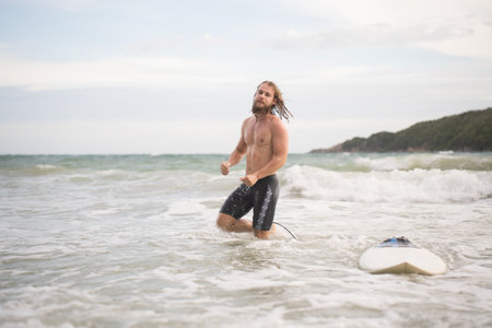 Portrait of a handsome young man with surfboard at the beachの写真素材