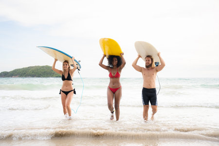 Rear view of two women and young man holding surfboards on their heads and walk into the sea to surf