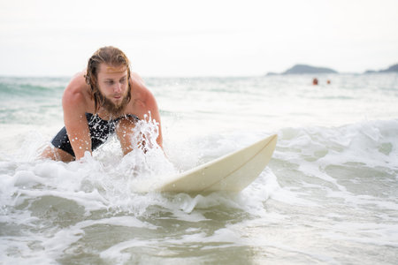 Young man surfing on the beach having fun and balancing on the surfboardの写真素材