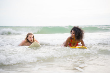 Young man and woman having fun with surfboard in the ocean on a sunny dayの写真素材
