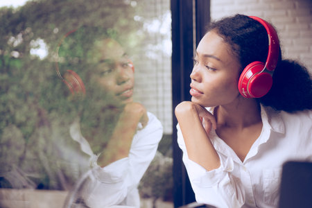 Beautiful young woman listening to music with headphones and drinking coffee in a cafÃ©