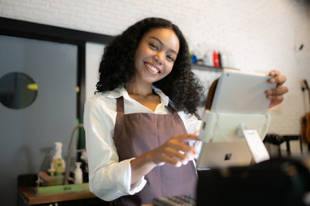 Portrait of smiling waitress using digital tablet in coffee shop with colleagues in background