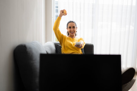 Happy young woman watching tv and cheering the game at home in the living room