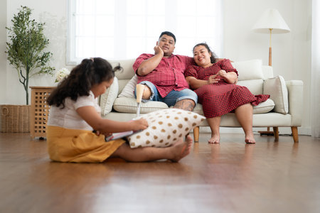 A plus size family with a father wearing a prosthetic leg, During rest time allow daughter to play games on tablet in the living room of the house.の写真素材