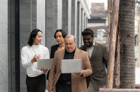 Group of business people walking and working on laptop computer in side of modern office building. Multiethnic group of business people using digital devices outdoor.の写真素材